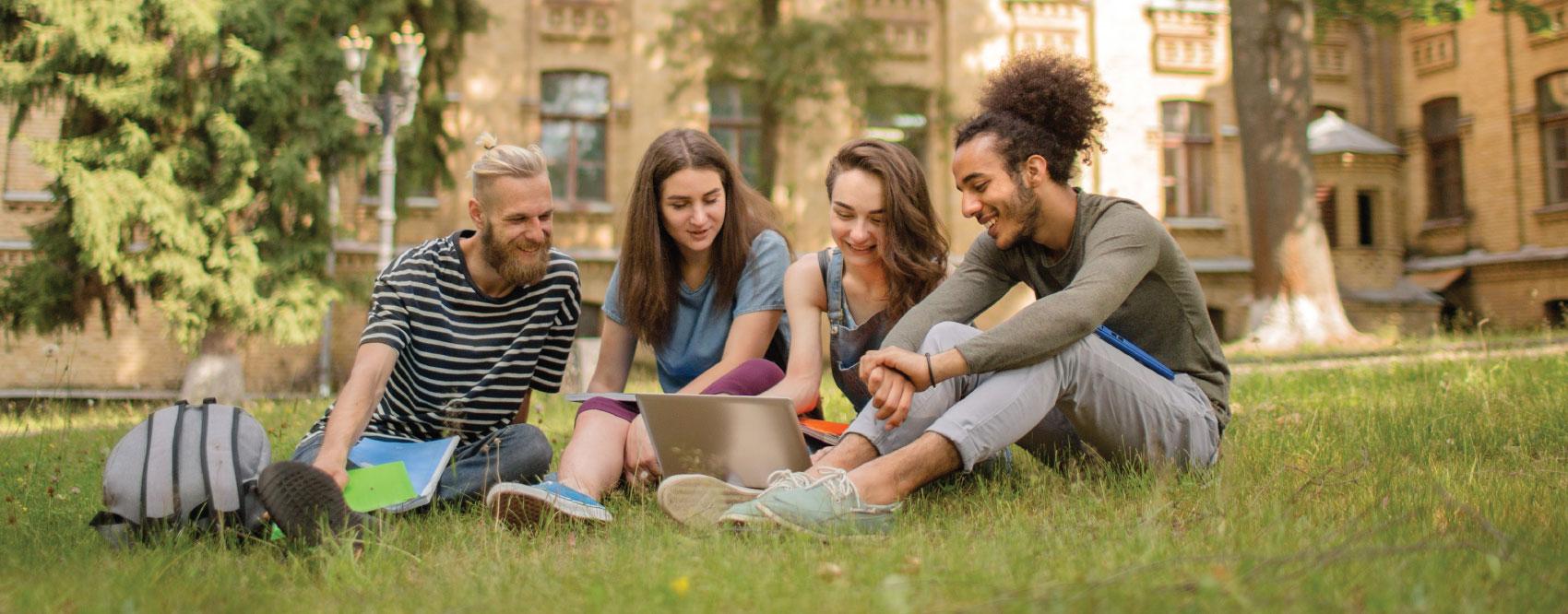 college students outside smiling sitting in the grass