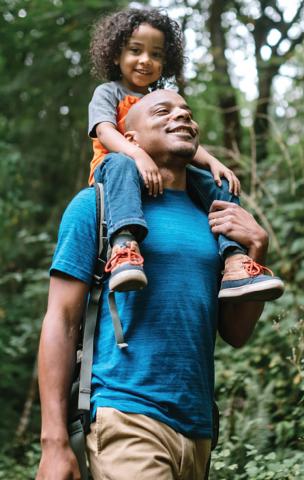 smiling child on fathers shoulders walking through the woods